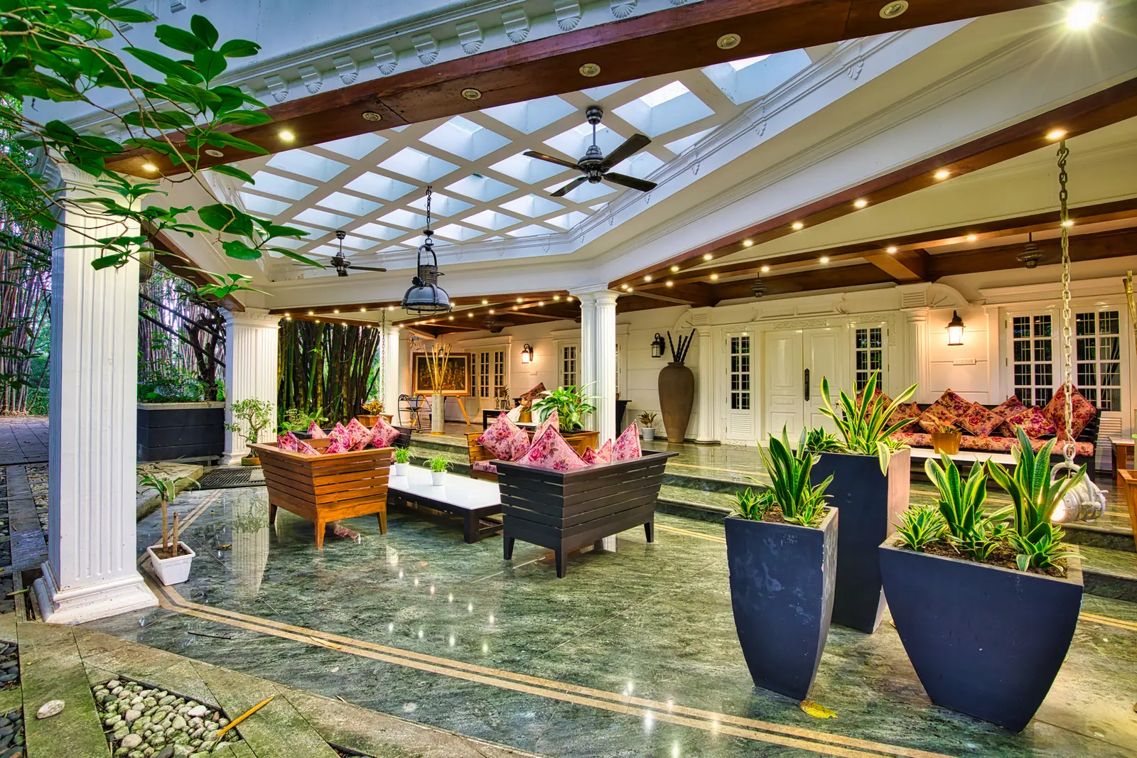 Open lounge with a skylight, swing seats and potted plants at a riverside Ayurveda retreat in Kerala