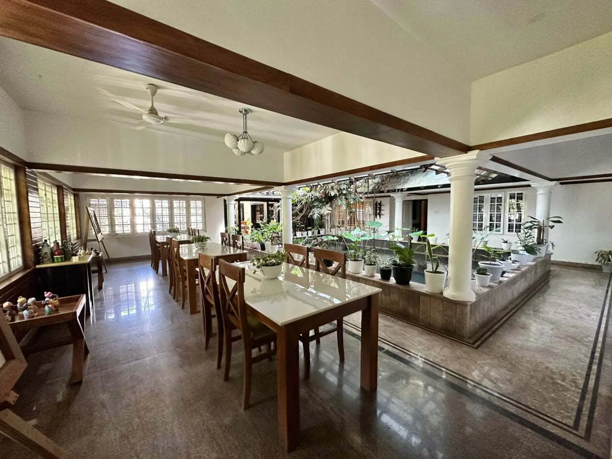 Dining hall with wooden tables beside an indoor courtyard garden at an Ayurveda retreat in Kerala