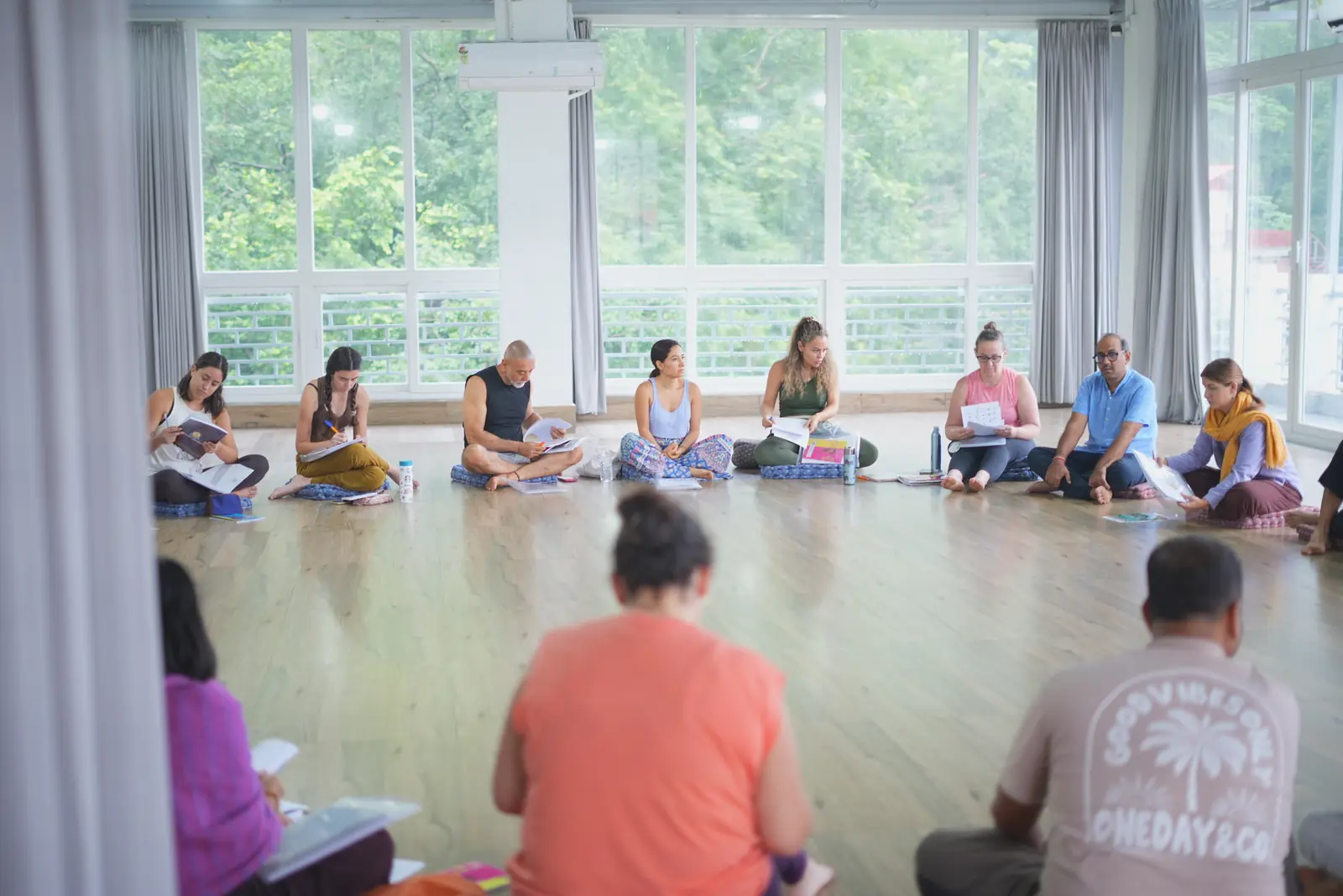 Yoga teacher training graduates in garlands around a flower rangoli in a yoga hall in Rishikesh