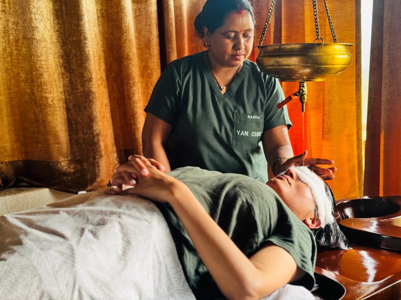Shirodhara therapy with warm oil poured from a brass vessel onto a guest's forehead in Rishikesh