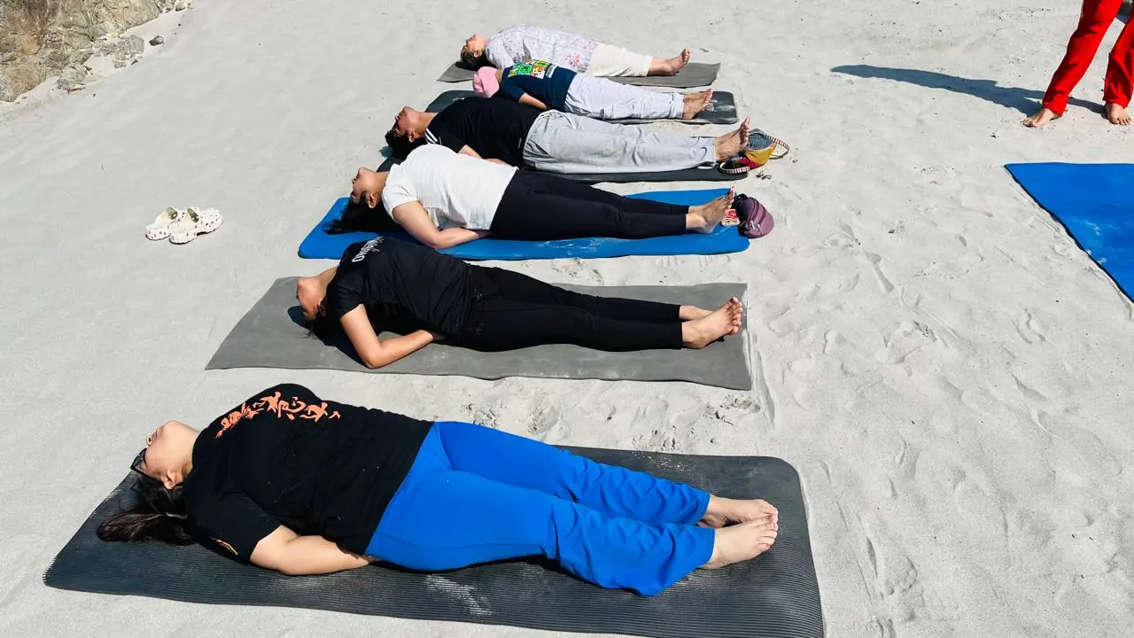 Small group stretching with yoga straps overhead in an indoor yoga hall in Rishikesh