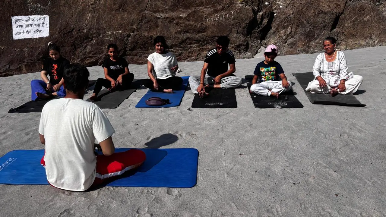 Small group stretching with yoga straps overhead in an indoor yoga hall in Rishikesh