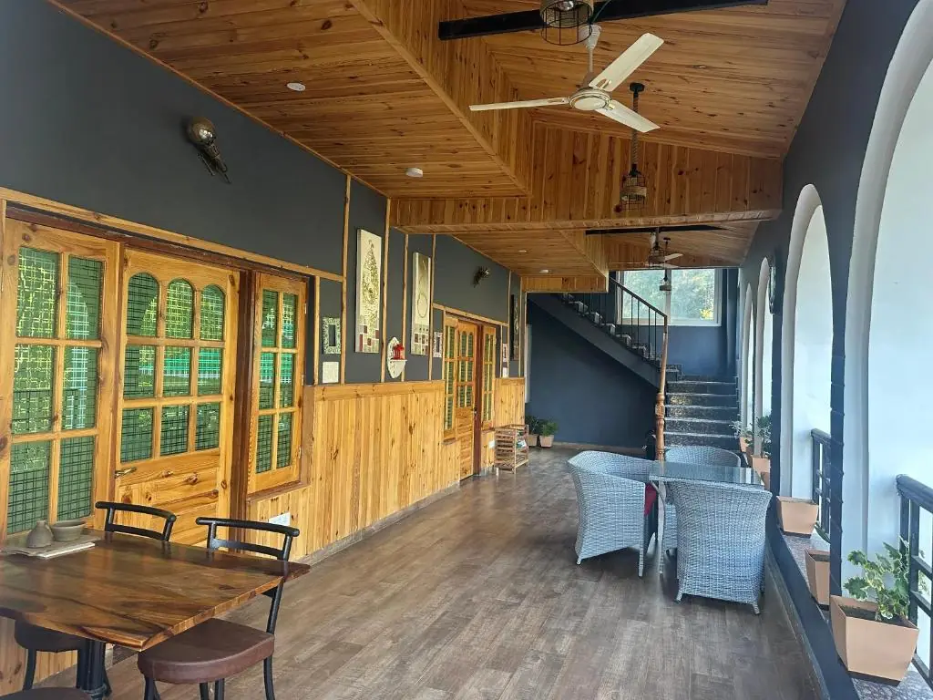 Hillside guesthouse with green roofs among trees below the snow-capped Dhauladhar range near Palampur